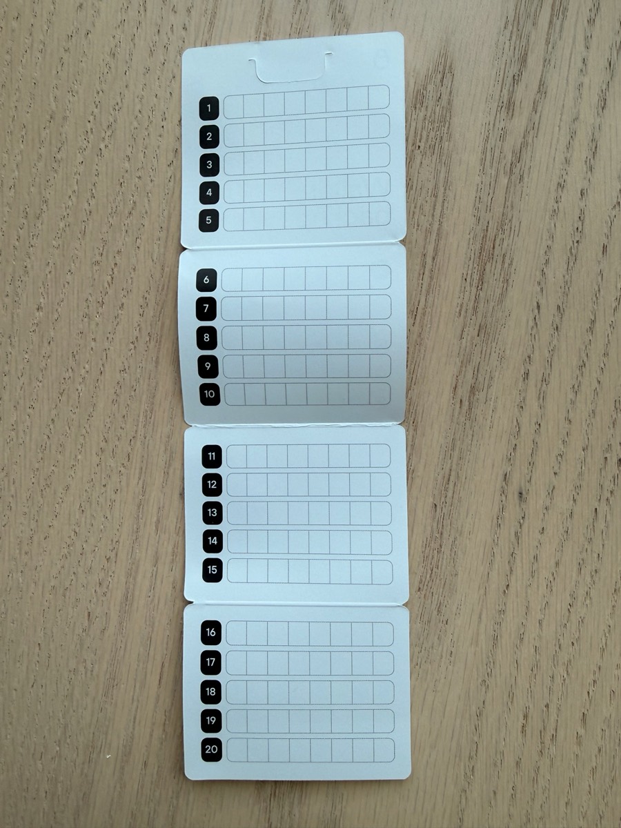 Four blank paper cards laid end-to-end on light wood, each with five rows of letter cells, numbered 1-5, 6-10, 11-15, and 16-20. The format matches a 20-word SLIP-39 share.